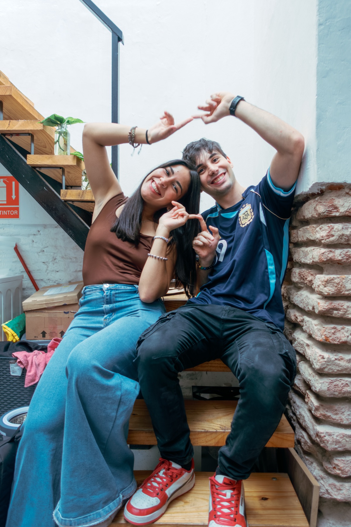 Dos amigos sentados en la escalera de la casa haciendo un corazón con las manos